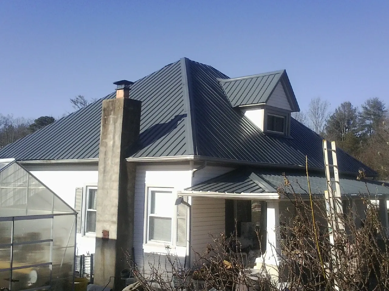 Dark blue standing seam metal roof on a white farmhouse with dormer — Slate & Tile Roof Repair by Roofing Brothers in Gateway