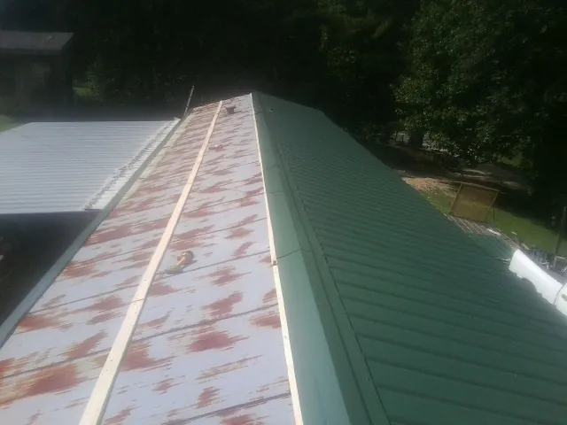 Old rusted panels beside newly installed green metal roofing — Wind Damage Roof Repair by Roofing Brothers in Gateway