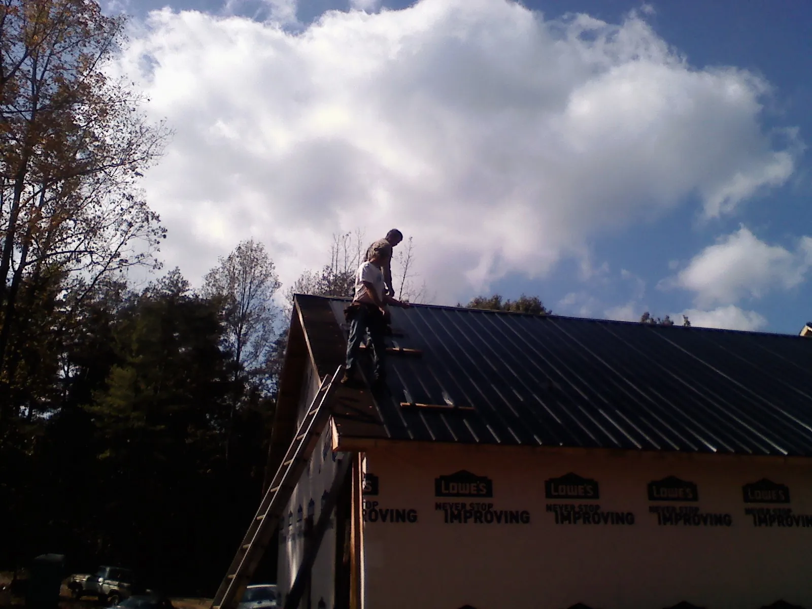 Roofer fastening dark metal panels high against a cloudy sky, from a Roof Inspection job in Gateway
